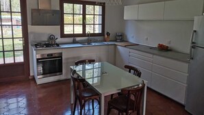 Una cocina moderna con armarios blancos, un refrigerador de acero inoxidable y una zona de comedor con una mesa de vidrio y sillas de madera.