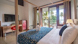 A hotel room with a bed, a desk, a television, and a view of palm trees. - Parangi Weligama Bay (Weligama)