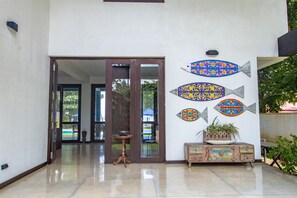 A hallway with a glass door leading to a patio area, a decorative fish wall art, and a wooden cabinet with a plant. - Parangi Weligama Bay (Weligama)