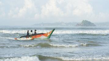 Un bote tradicional con pasajeros en un mar tranquilo, tierra distante con edificios y un cielo despejado.