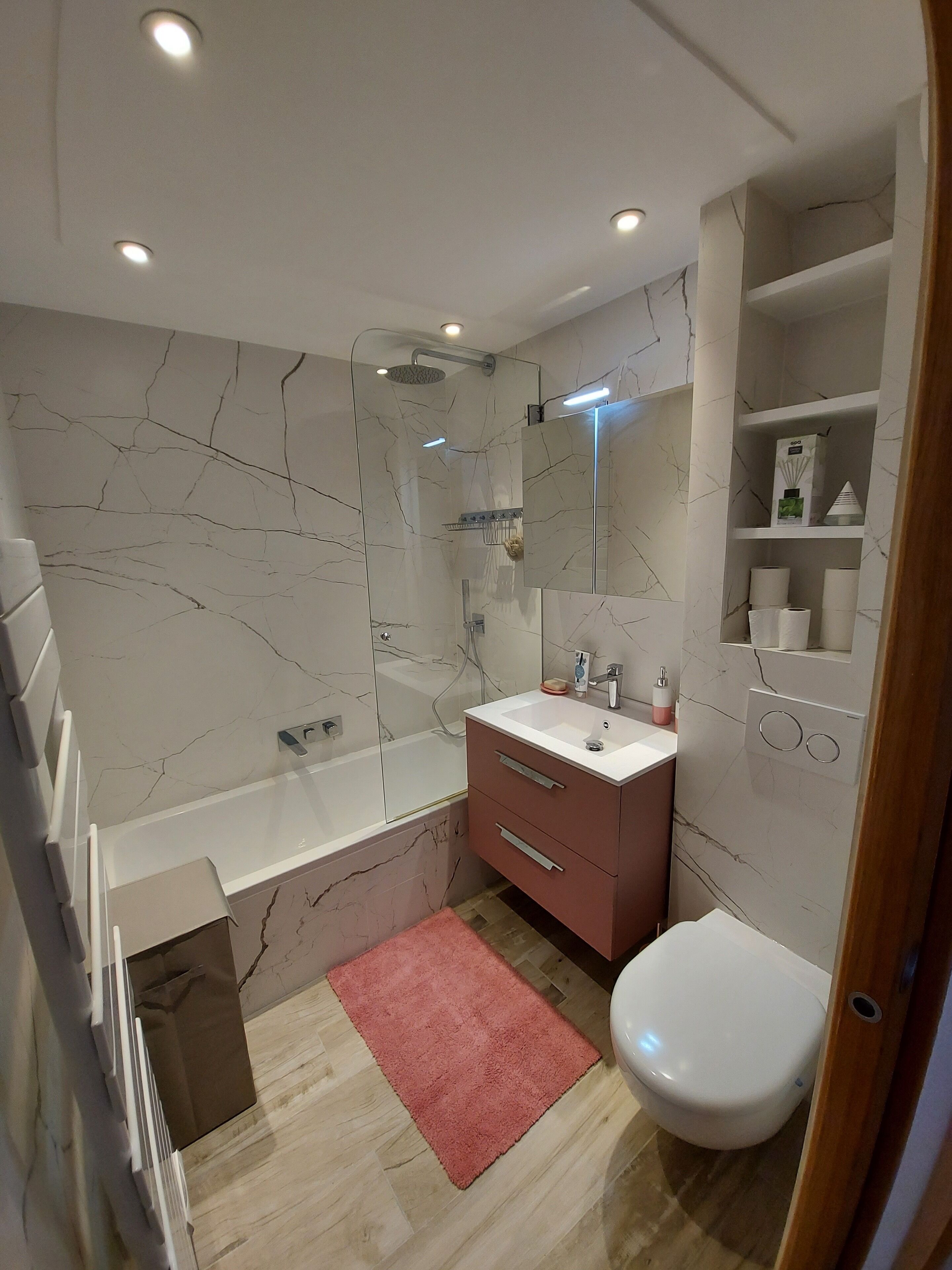 Une salle de bain moderne avec un pare-baignoire en marbre, une douche en verre, un lavabo blanc et un meuble-lavabo rose.