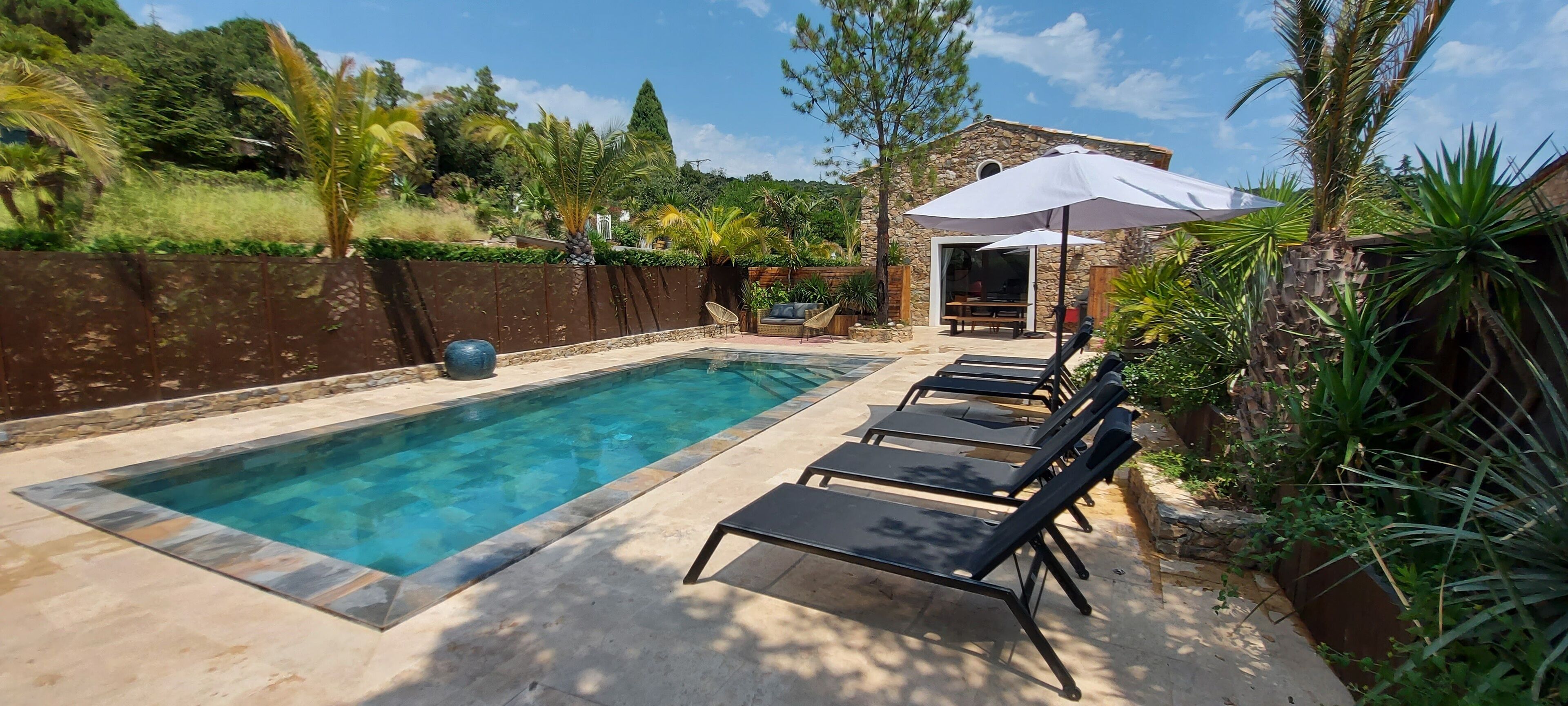 Une piscine rectangulaire bordée de pierres, entourée de chaises longues et d’un parasol.
