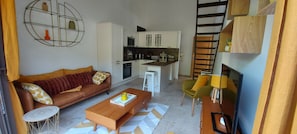 Un moderno salón con un sofá marrón, una mesa de centro de madera y una cocina con armarios blancos y un microondas.