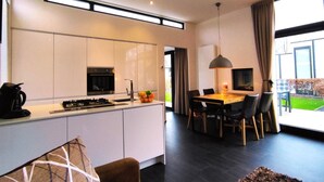 A modern kitchen with a built-in oven, a dining area with a table and chairs, and a large window offering a view of the outdoors.