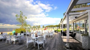 An outdoor dining area with white chairs and tables, overlooking a body of water.