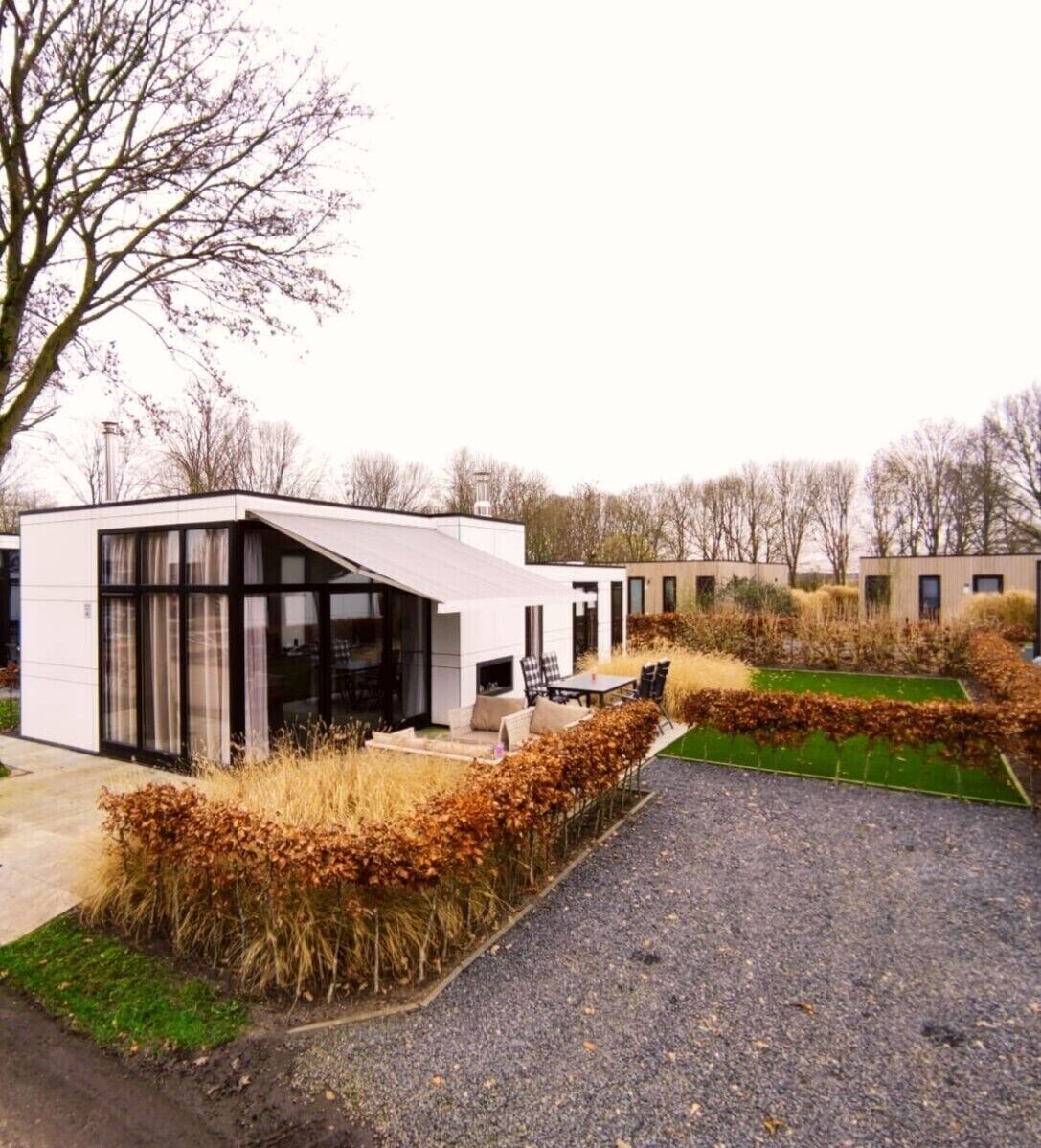 A modern building with a glass facade, a patio area with outdoor seating, and a well-maintained garden with hedges and grass.