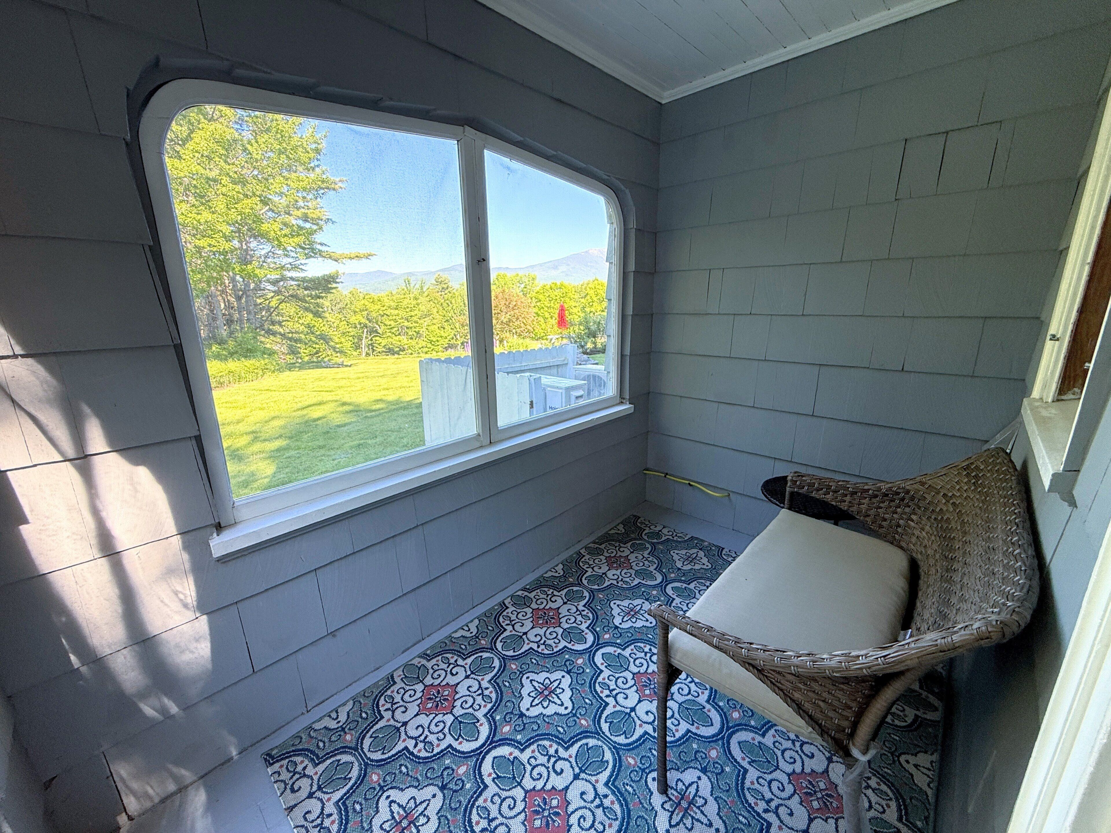 Une pièce dotée d’une grande fenêtre, d’un sol à motifs et d’un fauteuil en osier.