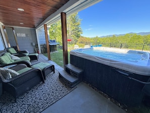 A covered patio with outdoor seating, a hot tub, and a view of a mountainous landscape.