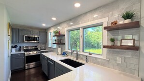 A modern kitchen with grey cabinets, stainless steel appliances, a large island, and a window with a view of greenery.