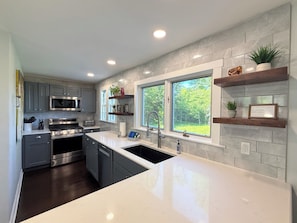 A modern kitchen with grey cabinets, stainless steel appliances, a large island, and a window with a view of greenery.