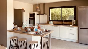 A modern kitchen with a central island, stainless steel appliances, and a large window. - Villa Marcassin 2021 classée 4*, 150 m2, piscine chauffée plage à 3 kms au calme (Messanges)