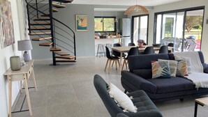 A modern living room with a dark blue sofa, a white dog resting on it, and a wooden staircase leading to an upper level. - Villa Marcassin 2021 classée 4*, 150 m2, piscine chauffée plage à 3 kms au calme (Messanges)