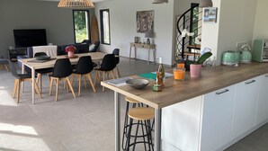 A modern kitchen with a central island, dining area with chairs, and a staircase leading to an upper level. - Villa Marcassin 2021 classée 4*, 150 m2, piscine chauffée plage à 3 kms au calme (Messanges)