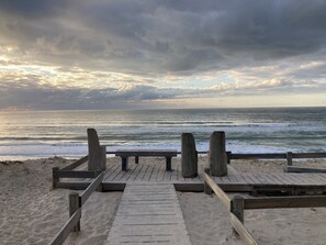 Een houten looppad dat naar het strand leidt, met een bankje en houten paaltjes.