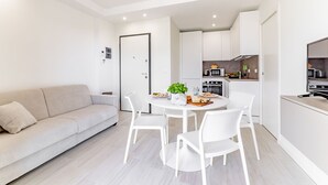 A modern, minimalist living room with a sofa, a dining table with chairs, and a kitchen area with cabinets and appliances. - Michelangelo - Borghetto Santo Spirito (Borghetto Santo Spirito)