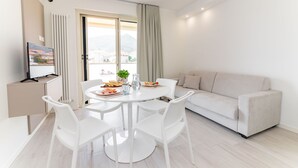 A modern living room with a round dining table, white chairs, a beige sofa, and a television on a cabinet. - Michelangelo - Borghetto Santo Spirito (Borghetto Santo Spirito)