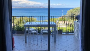 Ein Balkon mit Tisch und Stühlen, Blick aufs Meer und eine Tür zum Innenbereich.