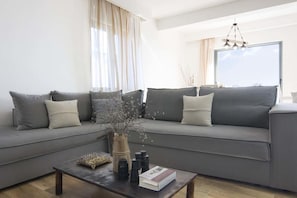 Relax in this serene living space with a comfortable sofa, coffee table, and natural light pouring in through large windows.