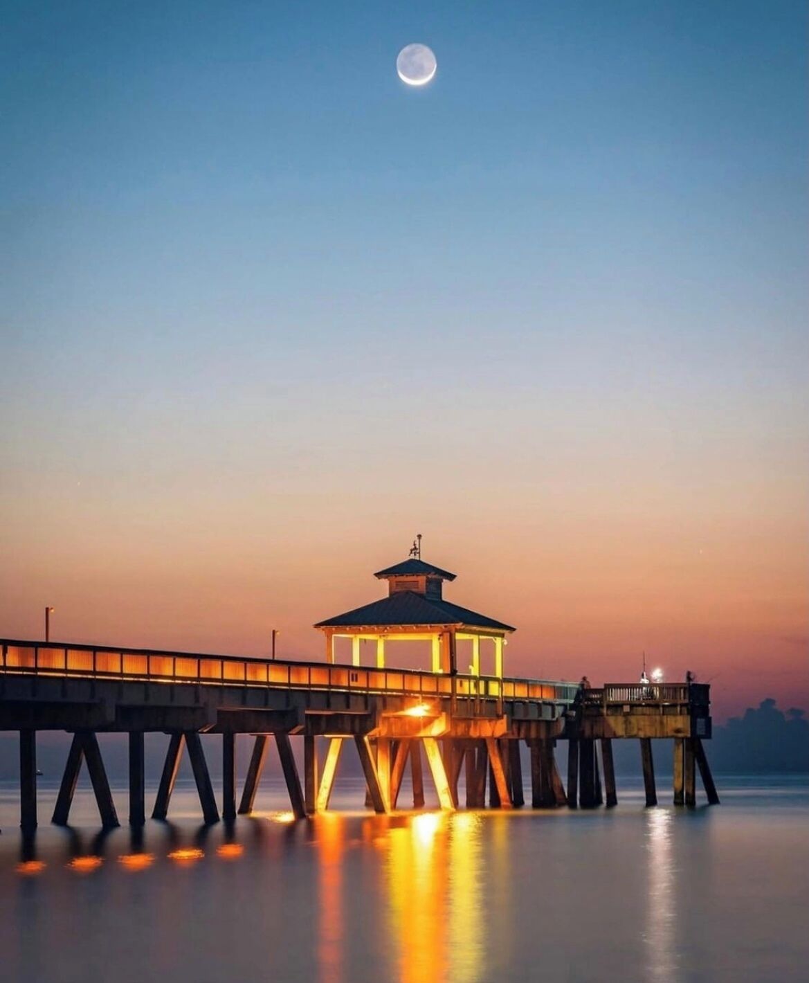 Un muelle se adentra en aguas tranquilas, con una pequeña estructura iluminada al final.