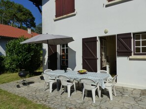 Eine Terrasse mit Tisch und Stühlen, einem Grill und einem überdachten Bereich mit Sonnenschirm.