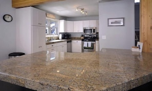 A kitchen with granite countertops, white cabinets, a microwave, an oven, and a coffee machine. - Bella View (Crested Butte)