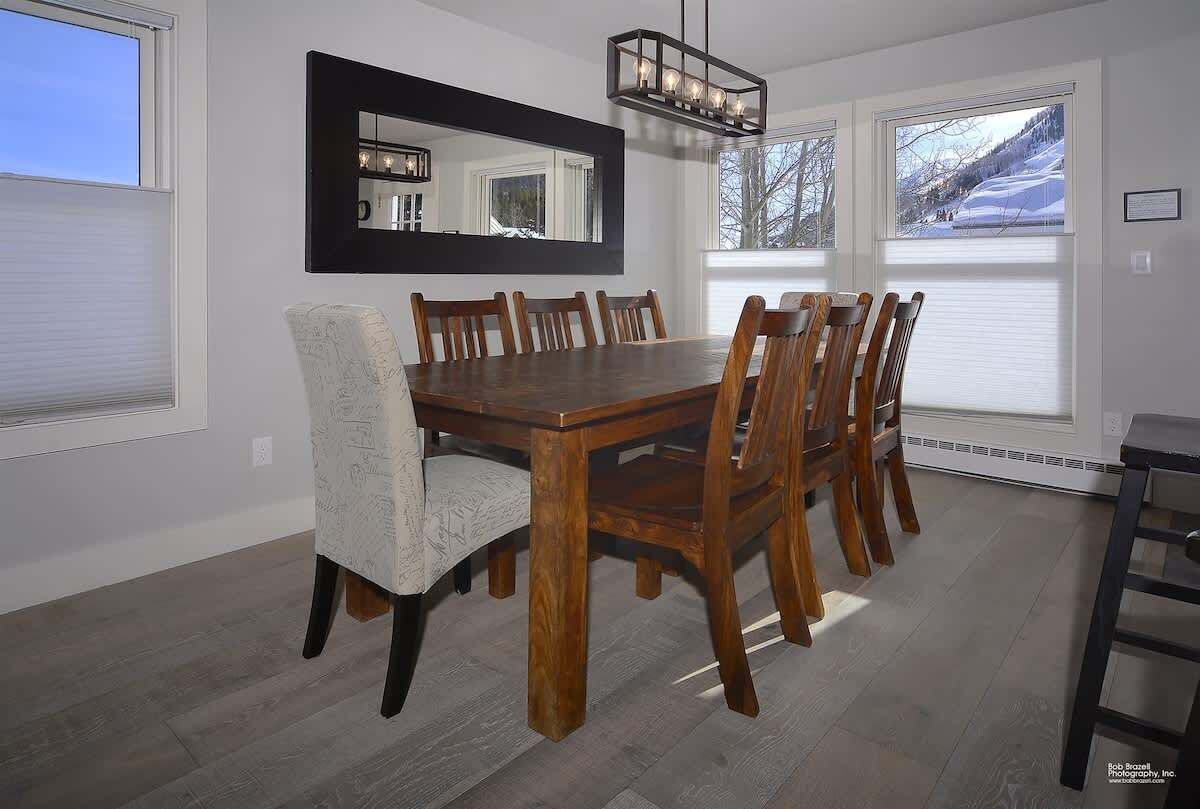 A dining room with a wooden table, six chairs, a large mirror, and a chandelier.