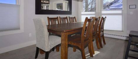 A dining room with a wooden table, six chairs, a large mirror, and a chandelier.