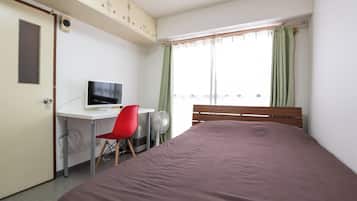 Un dormitorio con cama, escritorio con computadora, silla y ventana con cortinas.