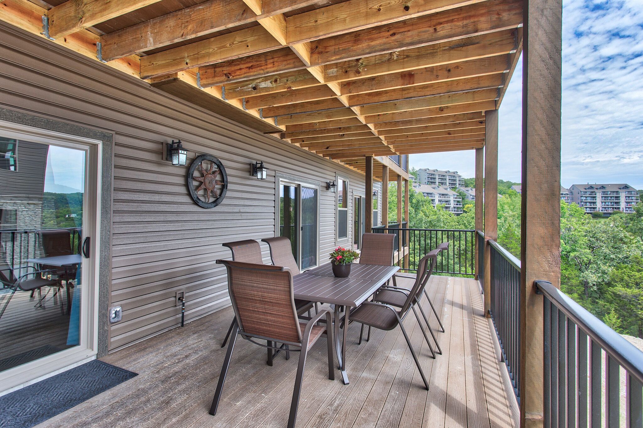 A covered deck with a table and chairs, a clock, and a view of buildings in the background.