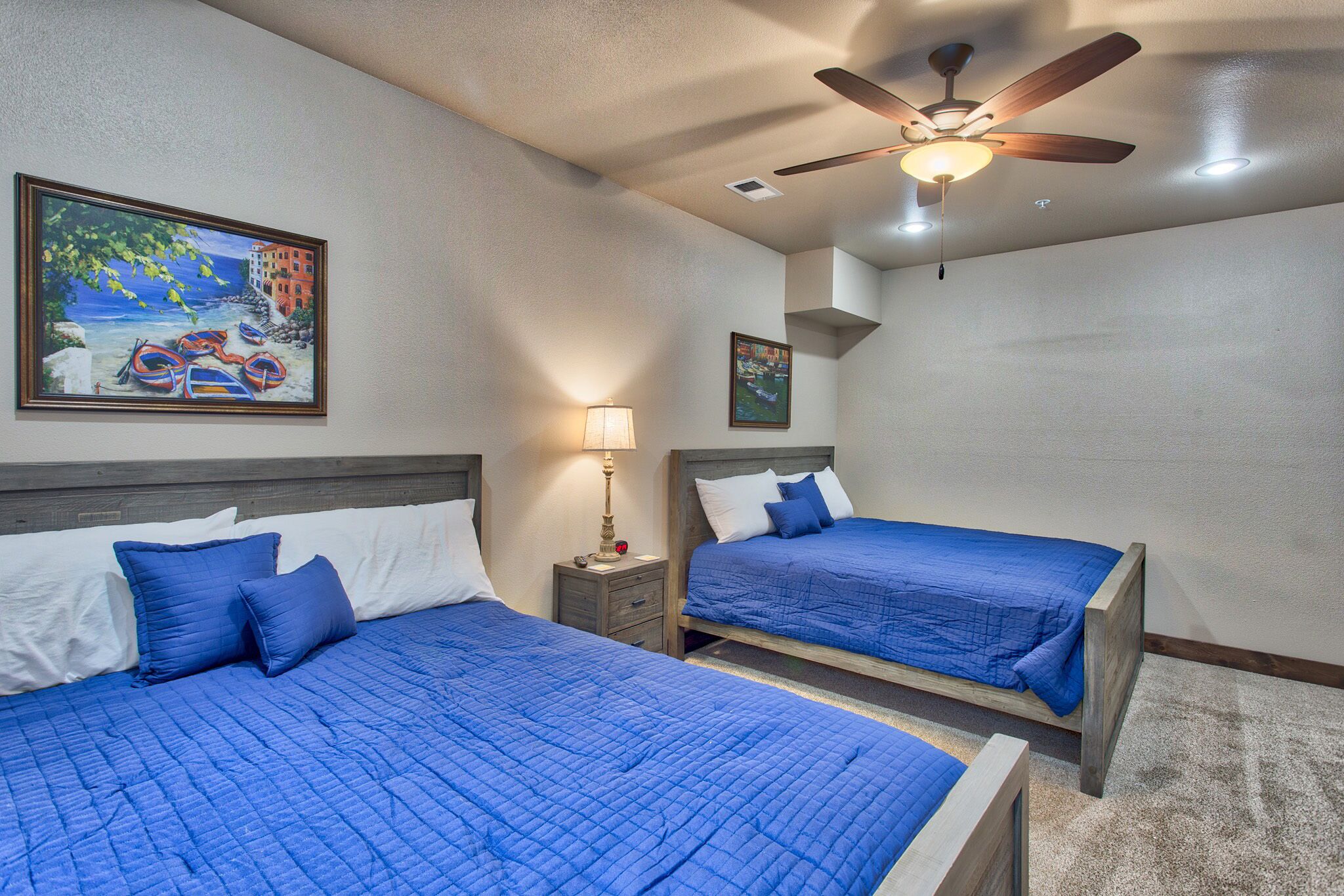 A hotel room with two beds, a ceiling fan, and artwork on the walls.