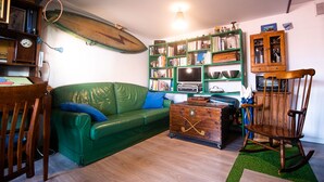 Un salón acogedor con un sofá verde, una mecedora de madera y una estantería llena de libros y objetos decorativos.