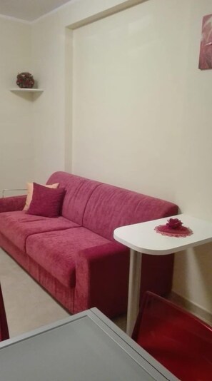Une petite pièce avec un canapé rouge, une petite table blanche et une chaise rouge.