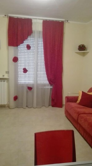 Un salon avec un canapé rouge, un fauteuil rouge et une petite table sur laquelle est posé un objet décoratif.