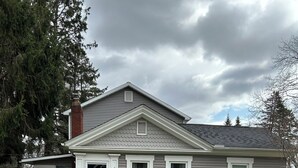 Una casa de dos plantas con porche delantero, chimenea y césped bien cuidado.