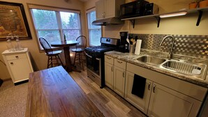 Cocina compacta con estufa, microondas y pileta. Cuenta con una mesa de comedor con sillas y un mueble pequeño.