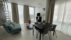 Un salon moderne comprenant un canapé, une table à manger avec des chaises, une petite table d’appoint avec une plante et un escalier.