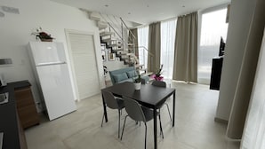 Une cuisine moderne avec un réfrigérateur blanc, une table à manger avec des chaises et un escalier menant à une mezzanine.