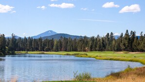Um campo de golfe com um lago, uma montanha ao fundo e uma área arborizada.