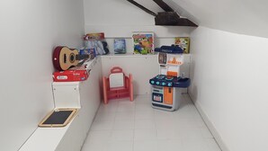 Une petite pièce bien aménagée, avec un mur blanc, une guitare rouge, un four miniature et un petit tabouret rouge.