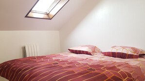 Une chambre avec un plafond en pente et un puits de lumière, comprenant un lit avec une literie à motifs et deux oreillers.