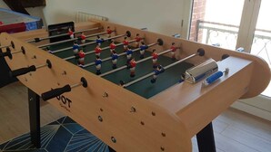 Une table de baby-foot avec un cadre en bois et des tiges en métal, située à l’intérieur et donnant sur un balcon.