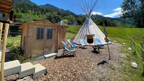 A wooden cabin and a teepee with lounge chairs in a rural setting. - Tepee at the Lama- & Alpakahof Triesenberg (Triesenberg)