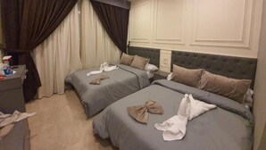 A hotel room with two beds, each with a grey bedspread and pillows, and a grey headboard. There is a desk with a chair and a bottle of hand sanitizer on it. - City Palace Hotel (Cairo)