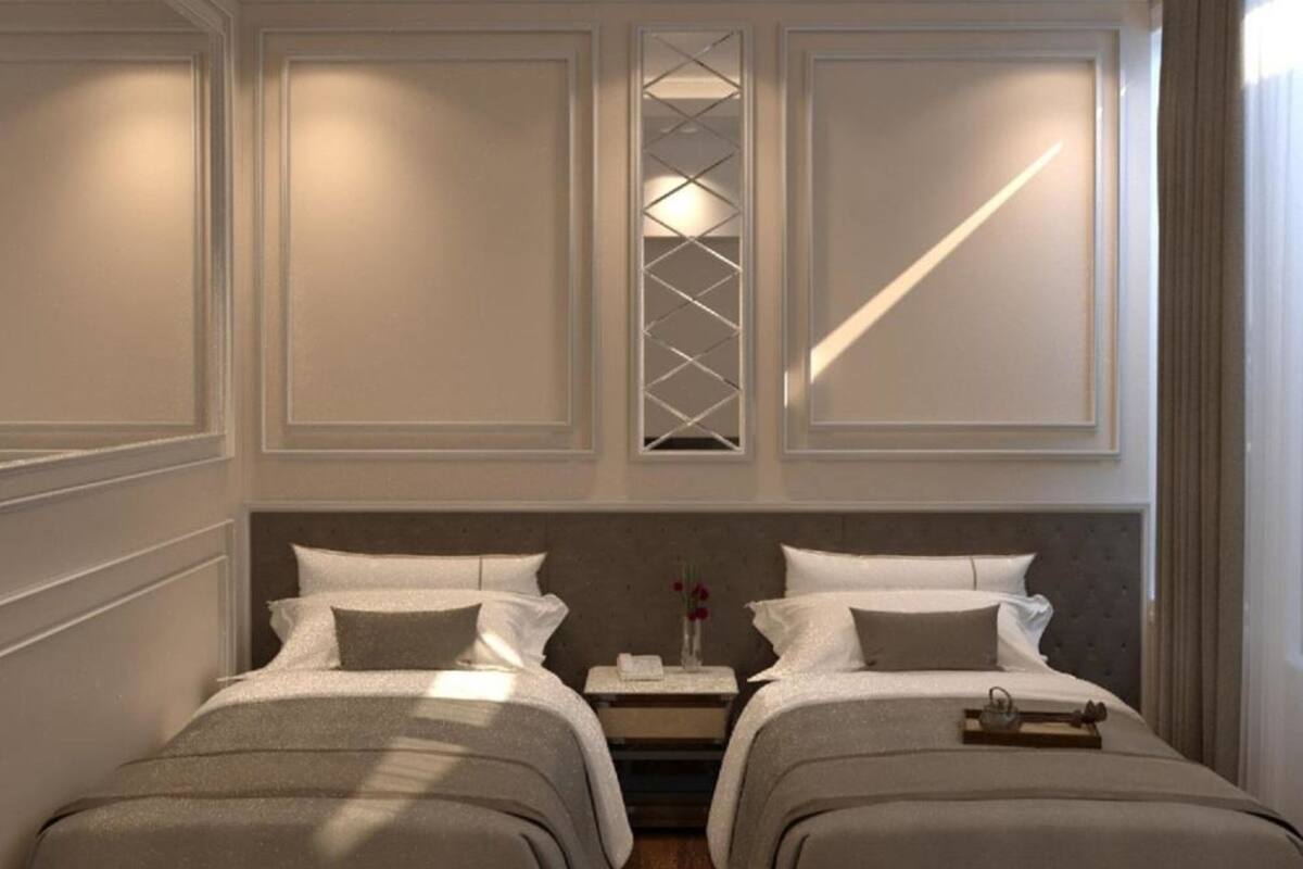 A hotel room with two beds, a nightstand, a decorative wall panel, and a window with a geometric pattern.