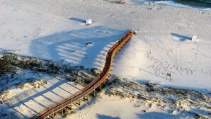 Pasarela de madera que lleva a una playa, con huellas de pasos y un letrero.