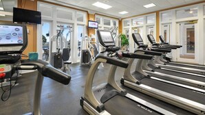 Un gimnasio con cintas de correr, equipo de ejercicio y una pantalla de televisión.
