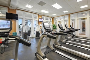A gym with treadmills, exercise equipment, and a TV screen.