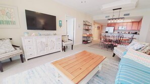 A living room with a TV, a dining area with a table and chairs, and a kitchen area with cabinets and a refrigerator.