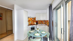 A compact kitchen with white cabinets, a tiled backsplash, and a dining area with a glass table and chairs. - 1 bedroom awesome apartment in Le Barcarès (Le Barcarès)