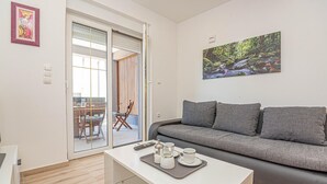 Una sala moderna con un sofá gris, una mesa de centro de vidrio con juego de té, y un cuadro de un arroyo en el bosque en la pared.